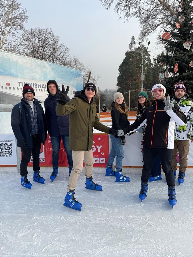 Un viaje en grupo de amigos de WeRoad posando para una foto en una pista de hielo al aire libre, llevando patines de hielo azules.