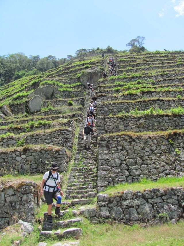 A WeRoad group trip hikes up a steep stone staircase built into grassy agricultural terraces on a mountainside.