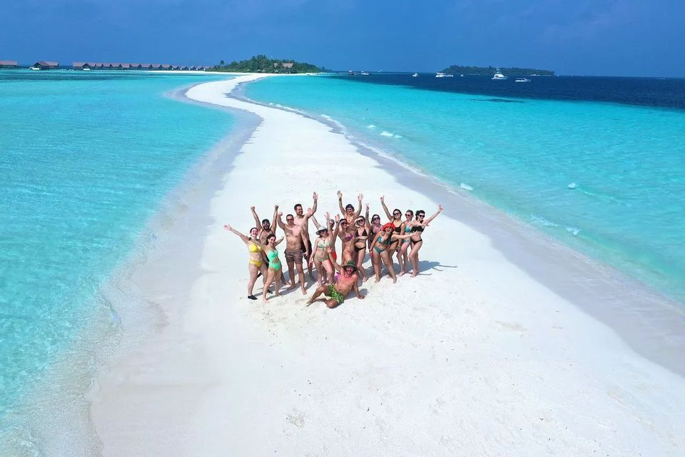 Eine WeRoad-Gruppe in Badebekleidung posiert auf einer langen weißen Sandbank, umgeben von klarem, türkisfarbenem Wasser.