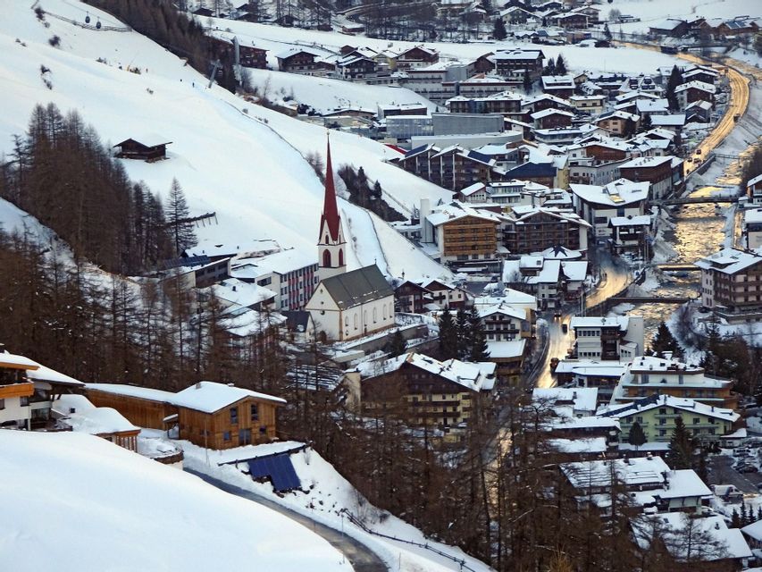 An alpine village with a red-steepled church sits in a snow-covered mountain valley.