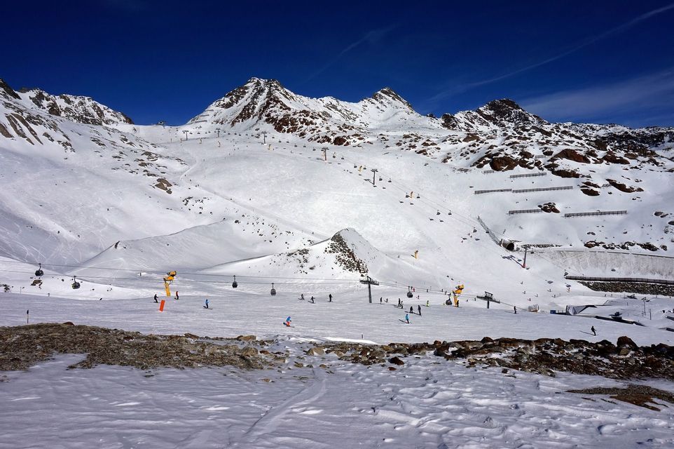 A panoramic view of a ski resort on a sunny day, with skiers on snowy slopes and chairlifts ascending the mountains.