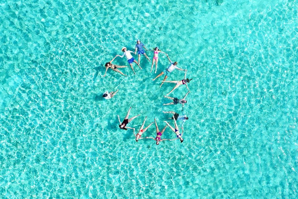 Un viaje en grupo de WeRoad tomados de las manos en círculo mientras flotan de espaldas en aguas claras de color turquesa.