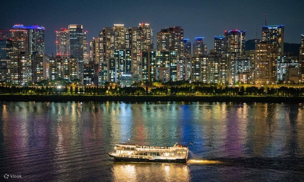 Una barca illuminata naviga di notte su un fiume, di fronte a uno skyline cittadino illuminato.