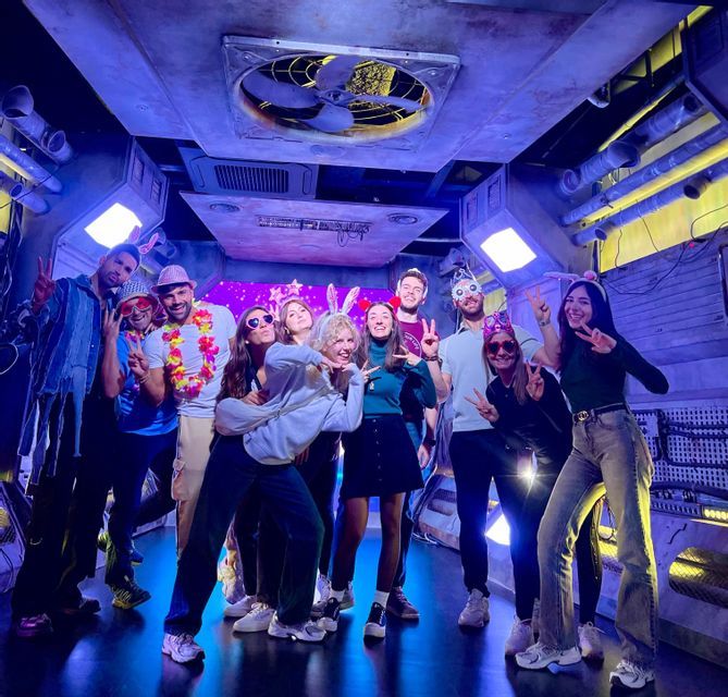 Un viaggio di gruppo WeRoad con persone che sorridono e posano con accessori da festa in una stanza a tema futuristico con luci blu.