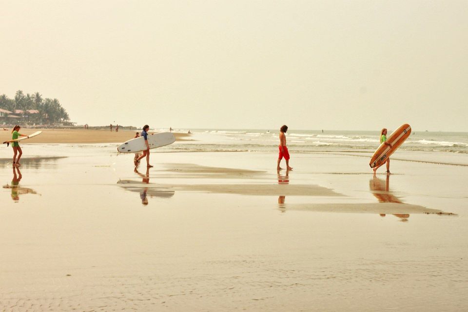 Un gruppo WeRoad di quattro persone con le tavole da surf cammina sulla sabbia bagnata di una spiaggia.