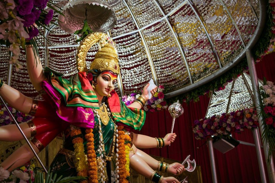 Un colorato idolo a più braccia della dea indù Durga, adornato con una corona d'oro e gioielli sotto un baldacchino sfarzoso e scintillante.