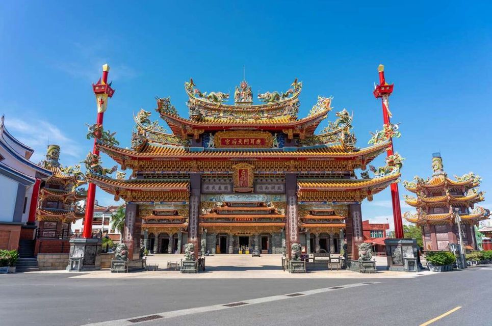 Un grande e ornato portale di un tempio dell'Asia orientale, con un tetto colorato e dettagliato, si erge al di là di una strada sotto un cielo azzurro e limpido.