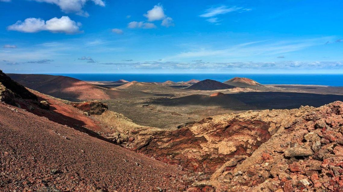 Una vista panorámica de un paisaje volcánico con cráteres de color marrón rojizo que conducen al océano azul bajo un cielo parcialmente nublado.