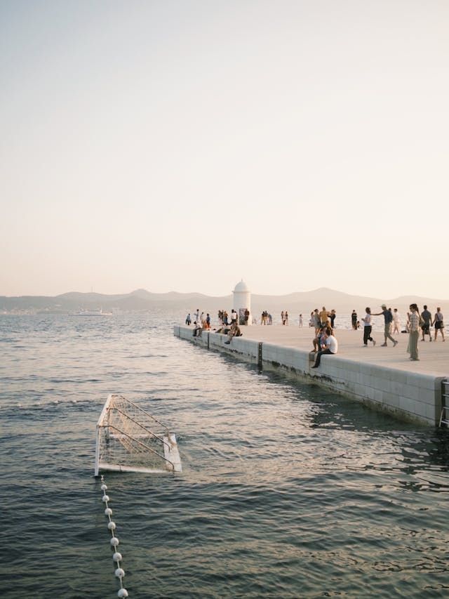 Eine WeRoad Gruppenreise auf einem langen Pier bei Sonnenuntergang, mit einem Wasserballtor, das im Meer schwimmt.