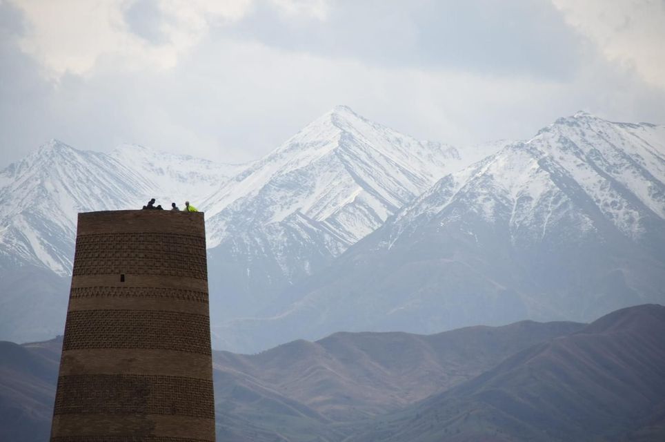 Un groupe WeRoad est perché au sommet d'une tour historique en briques, avec une vaste chaîne de montagnes enneigées en arrière-plan.