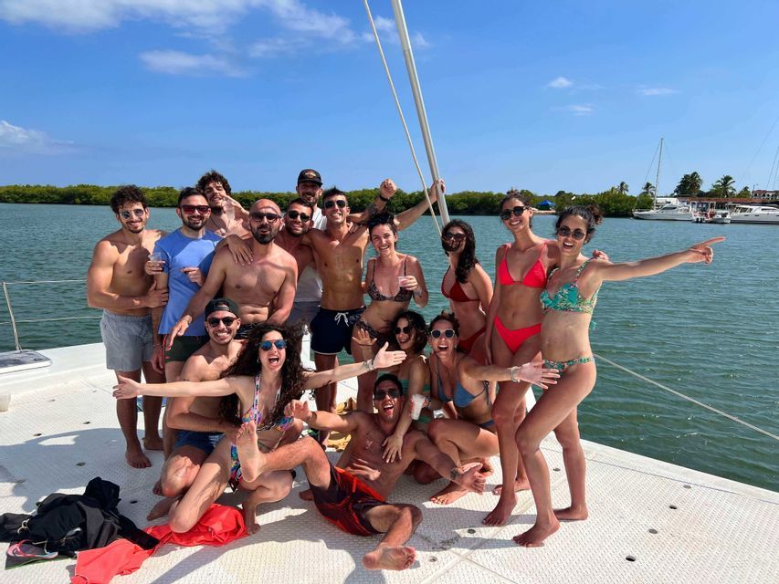 A WeRoad group trip of people in swimwear posing for a group photo on the deck of a catamaran on a sunny day.