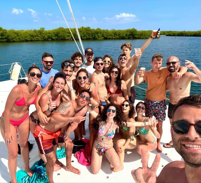 A WeRoad group trip smiling and posing for a group selfie on the deck of a boat on a sunny day.