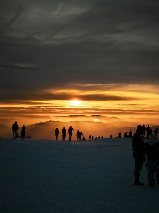 Silhouetten einer WeRoad-Gruppenreise auf einem verschneiten Bergrücken beim Sonnenaufgang über fernen Gipfeln
