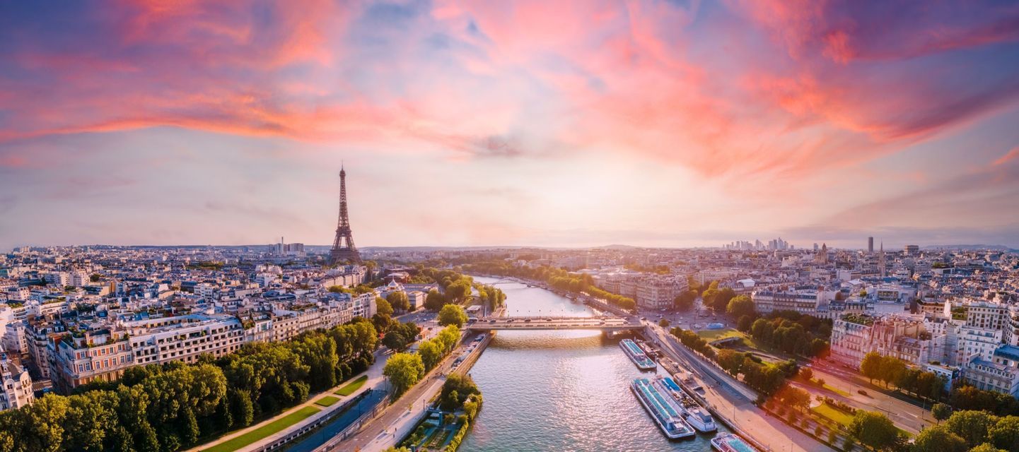 Una vista aerea dello skyline di Parigi con la Torre Eiffel e il fiume Senna sotto un tramonto drammatico rosa e arancione.