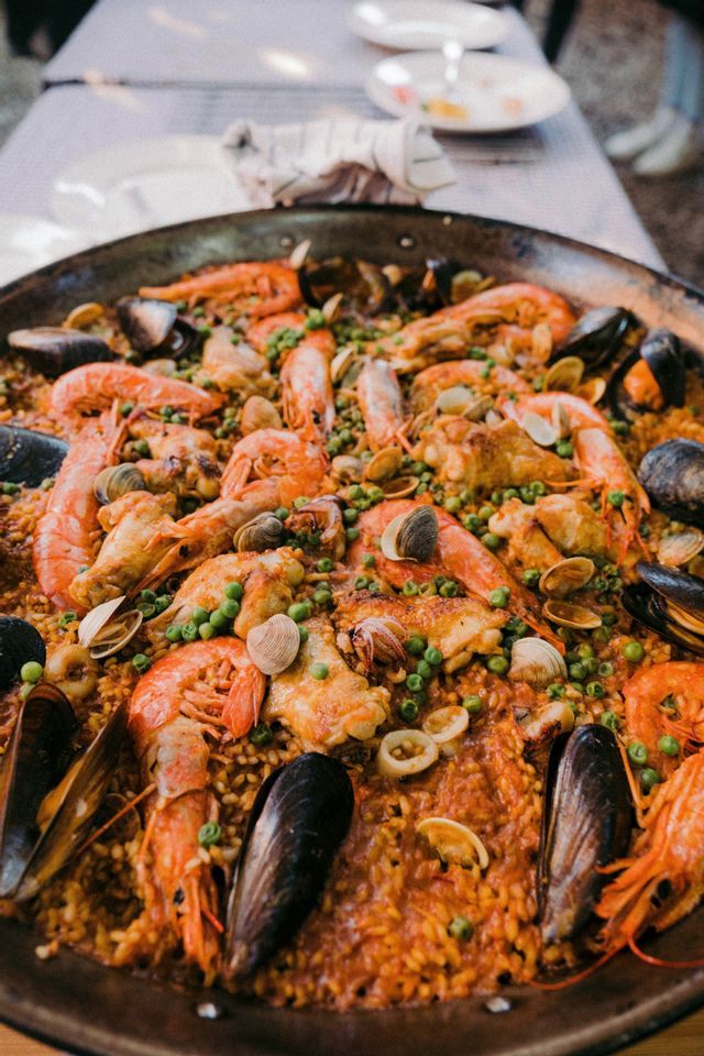 Primo piano di una paella tradizionale in una grande padella, ricca di riso, gamberi, cozze, pollo e piselli.
