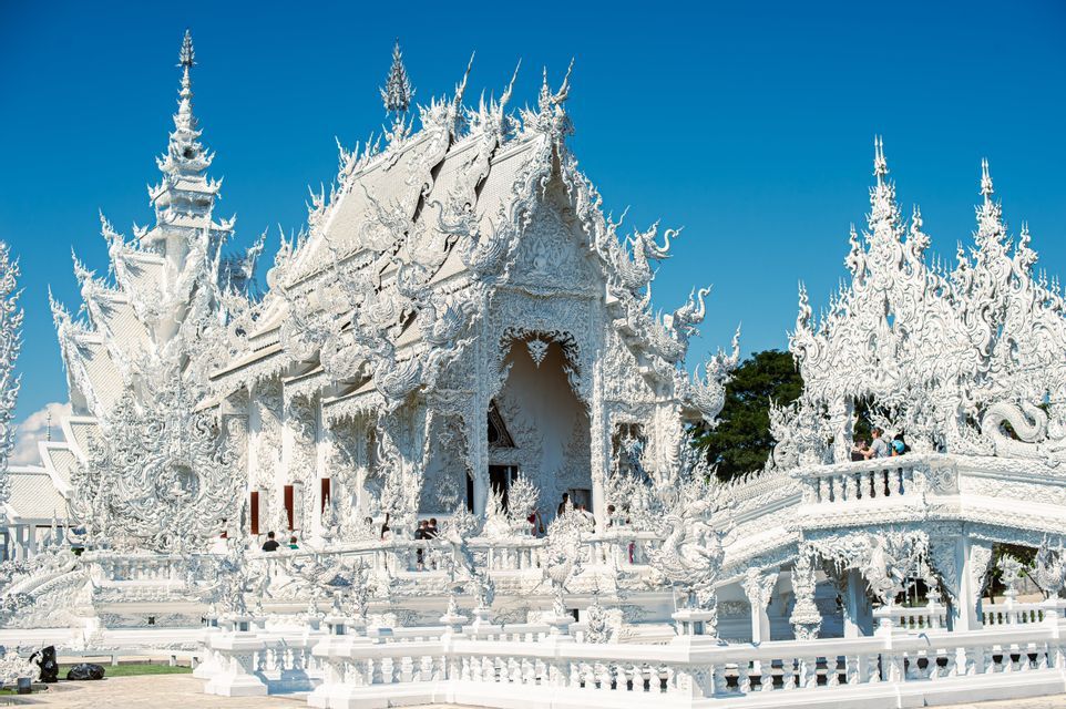 Un complexe de temples orné, tout de blanc, avec des sculptures et des flèches complexes, se dresse sous un ciel bleu profond et limpide.