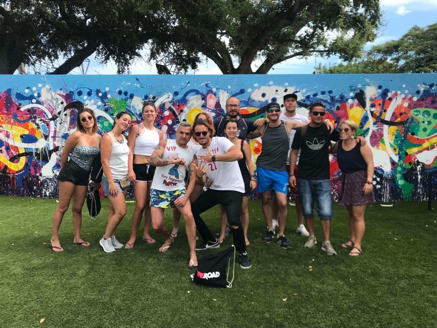 Un voyage de groupe WeRoad posant ensemble pour une photo sur une pelouse devant un mur de graffitis colorés.