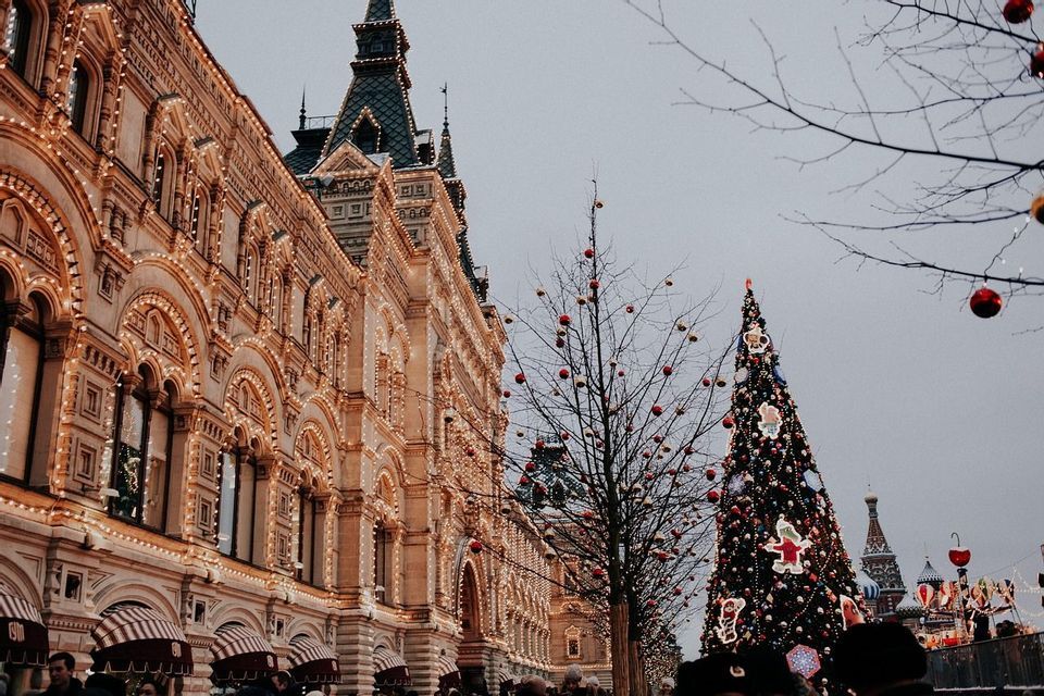 Un edificio decorato con luci accanto a un grande albero di Natale in piazza, sotto un cielo grigio.