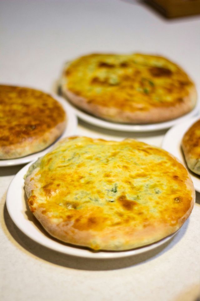 A close-up of several round, golden-baked cheese and herb breads on white plates arranged on a table.