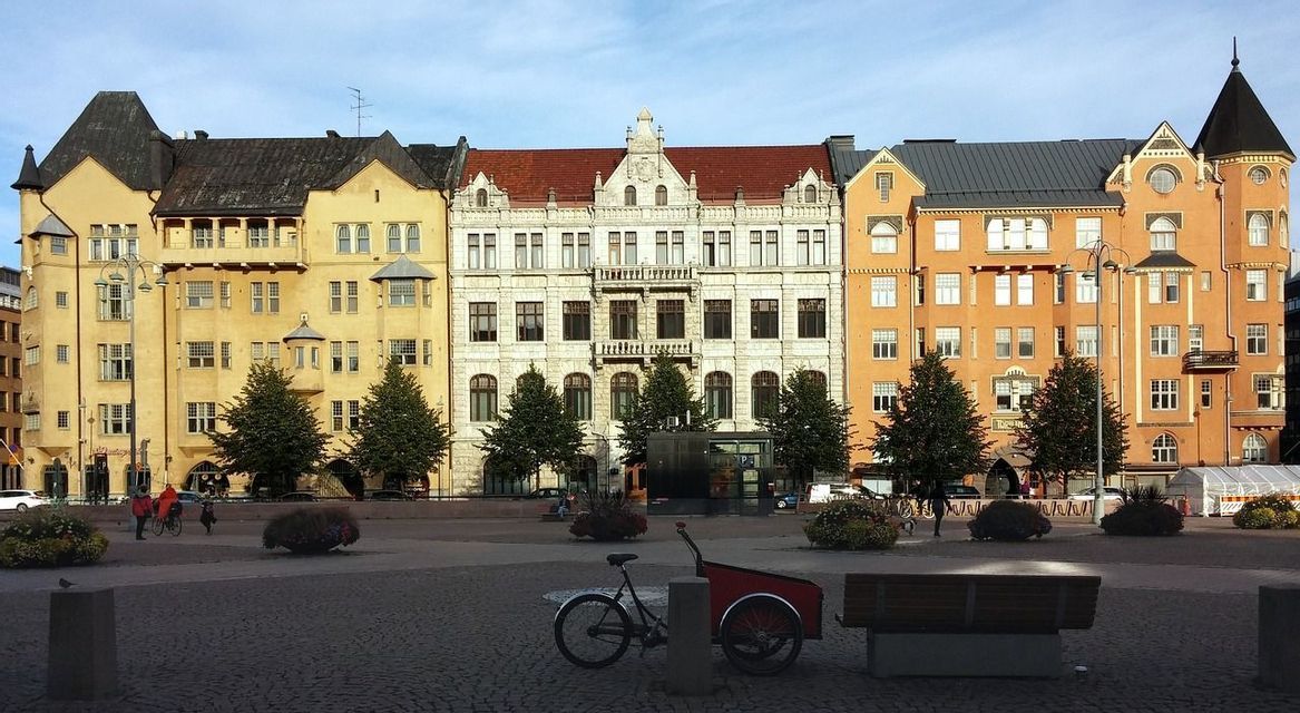 Una fila di edifici storici colorati si affaccia su una piazza cittadina acciottolata con una bici da carico parcheggiata in primo piano.