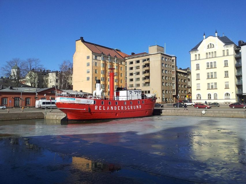 Una nave rosso brillante chiamata Relandersgrund ha attraccato in un porto cittadino parzialmente ghiacciato in una giornata di sole con gli edifici sullo sfondo.