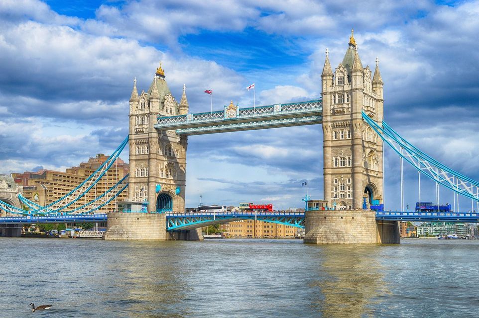 L'iconico Tower Bridge con le sue due torri che attraversano il Tamigi in una giornata luminosa e nuvolosa, mentre gli autobus rossi passano.