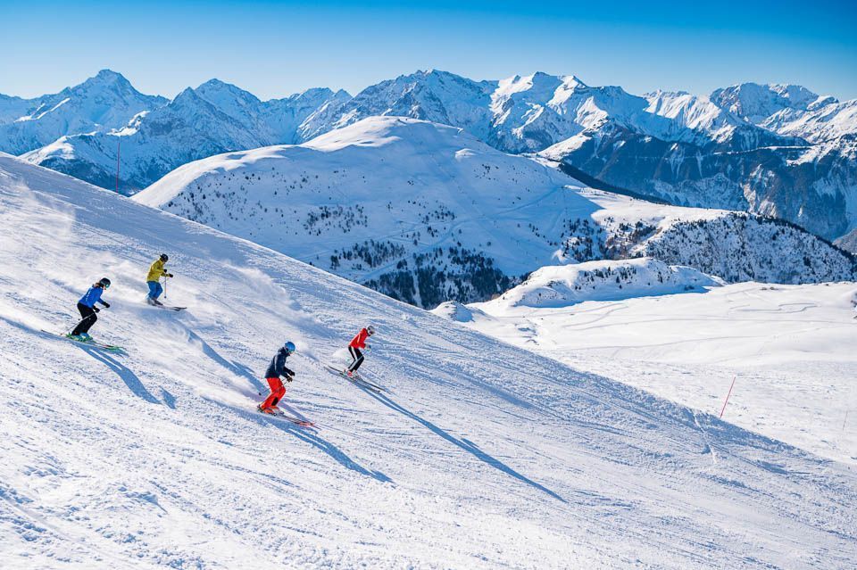 Eine WeRoad Gruppenreise beim Skifahren auf einem sonnigen, schneebedeckten Berghang, mit einer weiten Bergkette im Hintergrund.