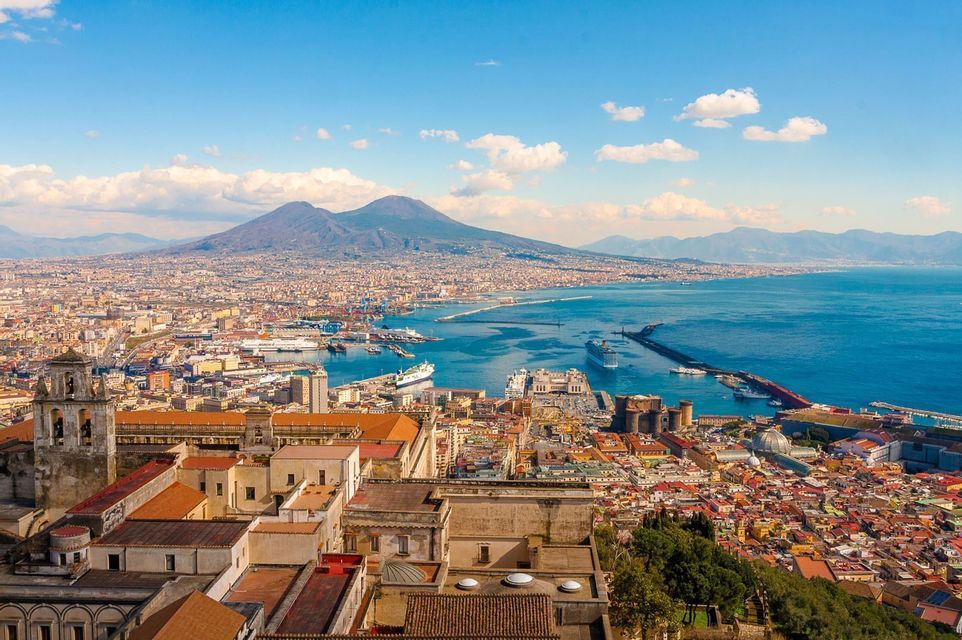 Une vue aérienne d'une ville côtière dense et de son port, avec un grand volcan s'élevant à l'arrière-plan sous un ciel bleu.