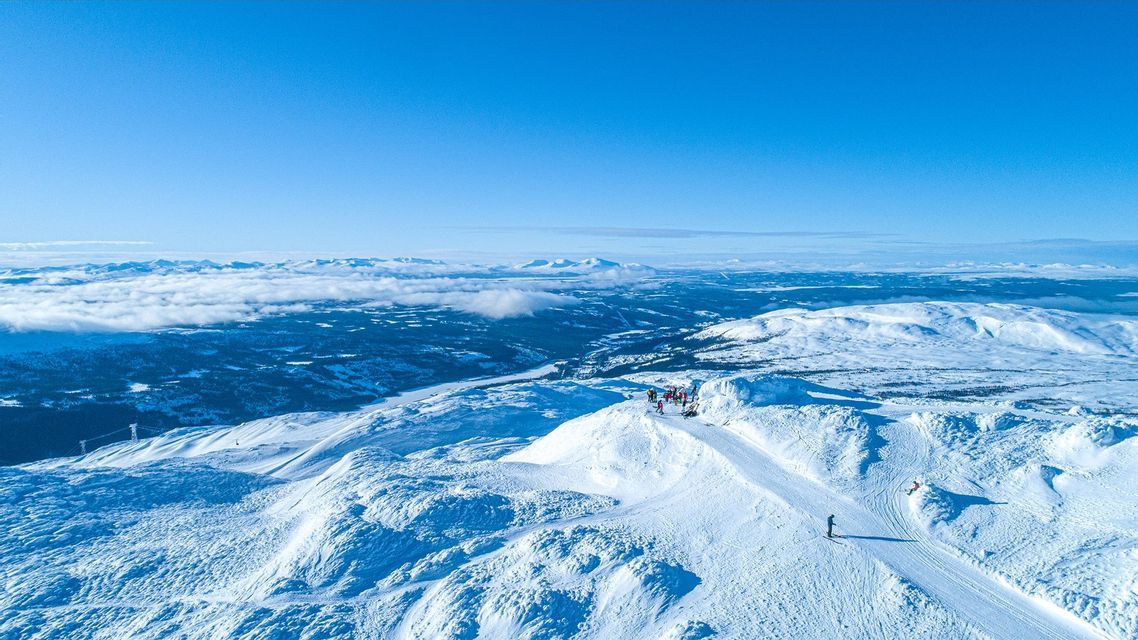 Una vista aerea di un viaggio di gruppo WeRoad su una cima di montagna innevata, che si affaccia su un vasto paesaggio invernale illuminato dal sole sotto un cielo azzurro e limpido.