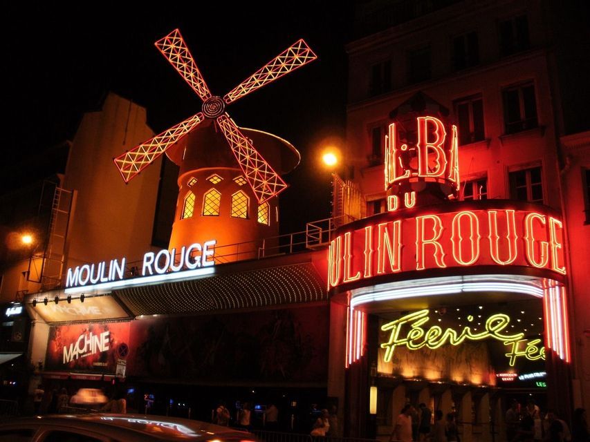 Le bâtiment du cabaret du Moulin Rouge la nuit, avec son iconique moulin rouge et son entrée illuminés par des néons rouges vifs.