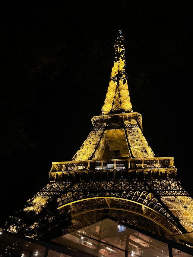 Une vue en contre-plongée de la Tour Eiffel illuminée de lumières dorées sur un ciel de nuit sombre.