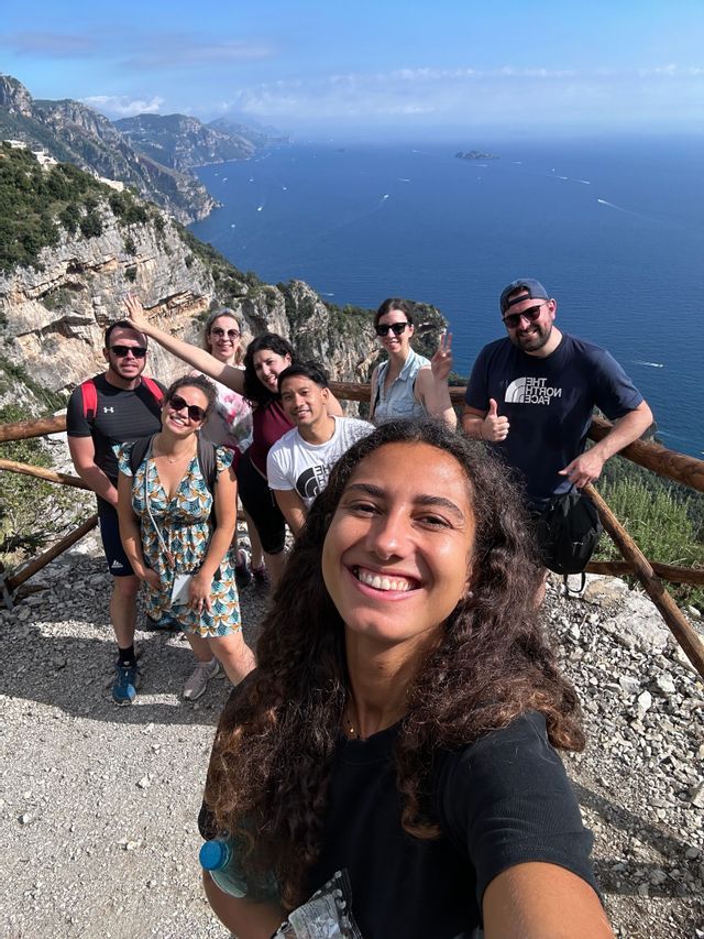 Un groupe WeRoad prend un selfie depuis un belvédère en bord de falaise, offrant une vue sur la mer et une côte déchiquetée.