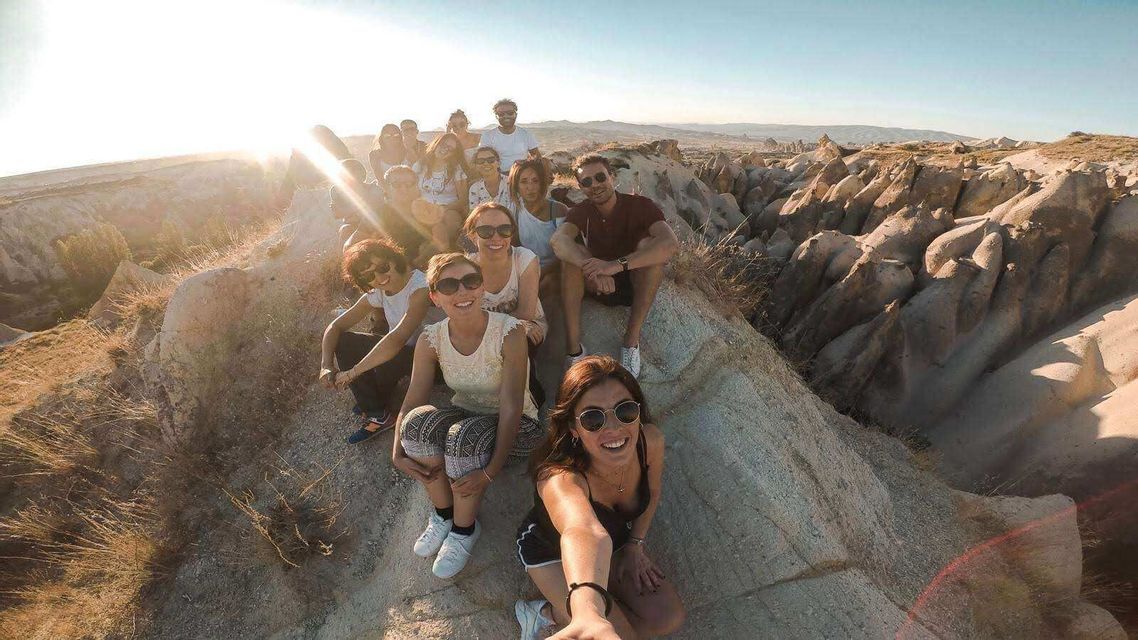 Un grupo de WeRoad sonríe para una selfie, sentado en una cresta rocosa con vistas a un cañón soleado.