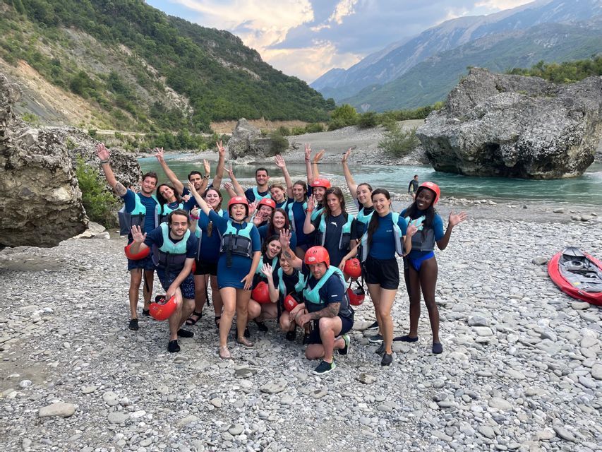 Un groupe WeRoad, équipé de gilets de sauvetage et de casques rouges, pose pour une photo sur une berge rocheuse au bord d'une rivière turquoise.