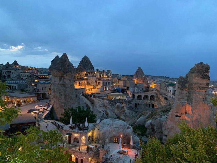 Un borgo incastonato in particolari formazioni rocciose, illuminato da luci calde sotto un cielo serale blu.