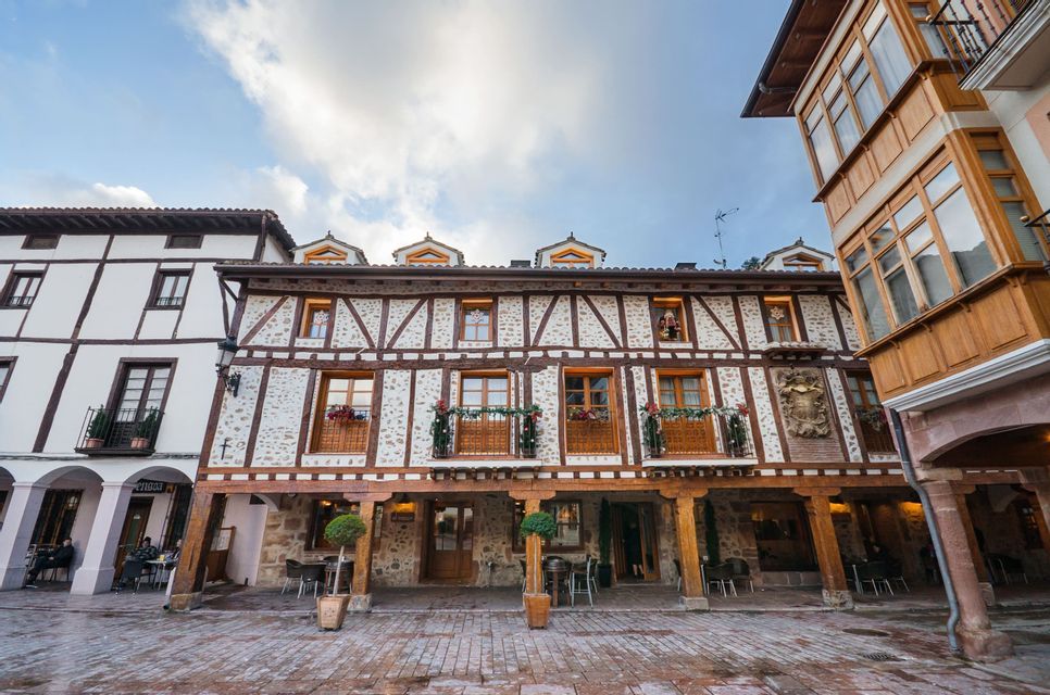 Prise de vue en contre-plongée d&#39;un bâtiment traditionnel à colombages avec une arcade, situé sur une place pavée sous un ciel bleu avec des nuages.