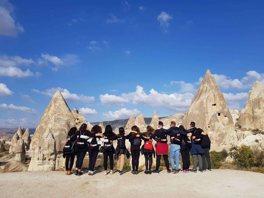 Vue de dos d'un voyage de groupe WeRoad, bras dessus dessous, admirant des formations rocheuses coniques sous un ciel bleu.