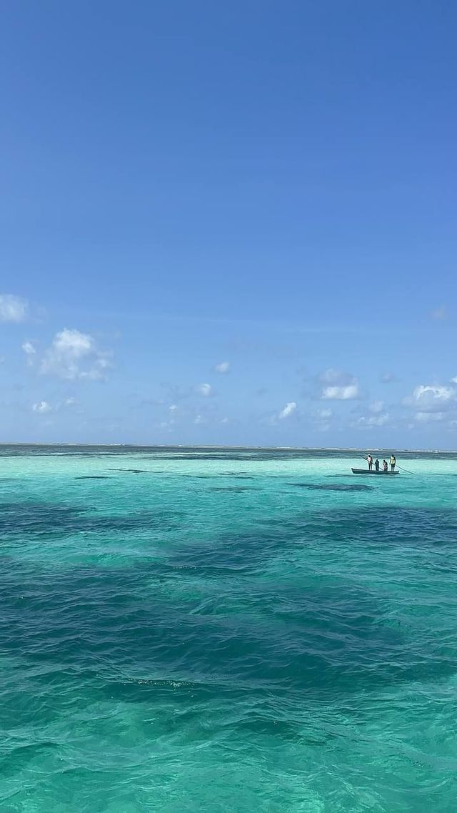 Un viaggio di gruppo WeRoad su una piccola barca che galleggia su un vasto oceano turchese, sotto un cielo azzurro limpido con nuvole leggere.