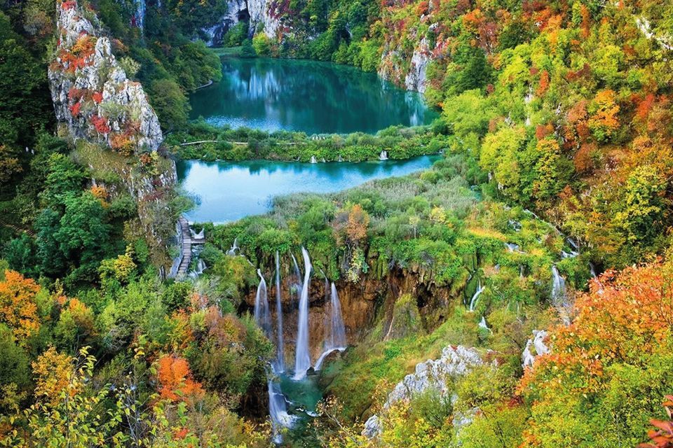 Waterfalls cascade into turquoise lakes surrounded by a dense forest with colorful autumn foliage.