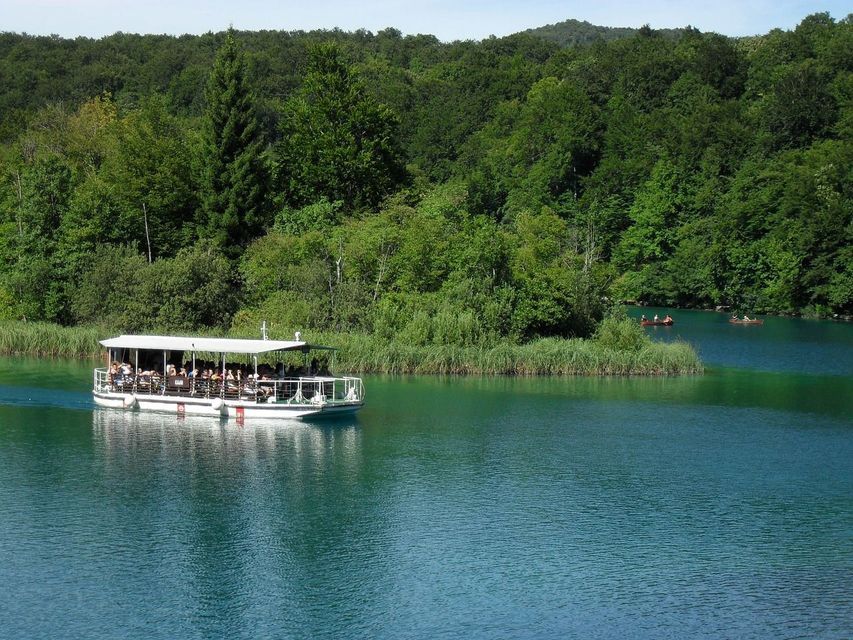 Un viaggio di gruppo WeRoad su una barca bianca naviga su un lago turchese, circondato da una lussureggiante foresta verde.