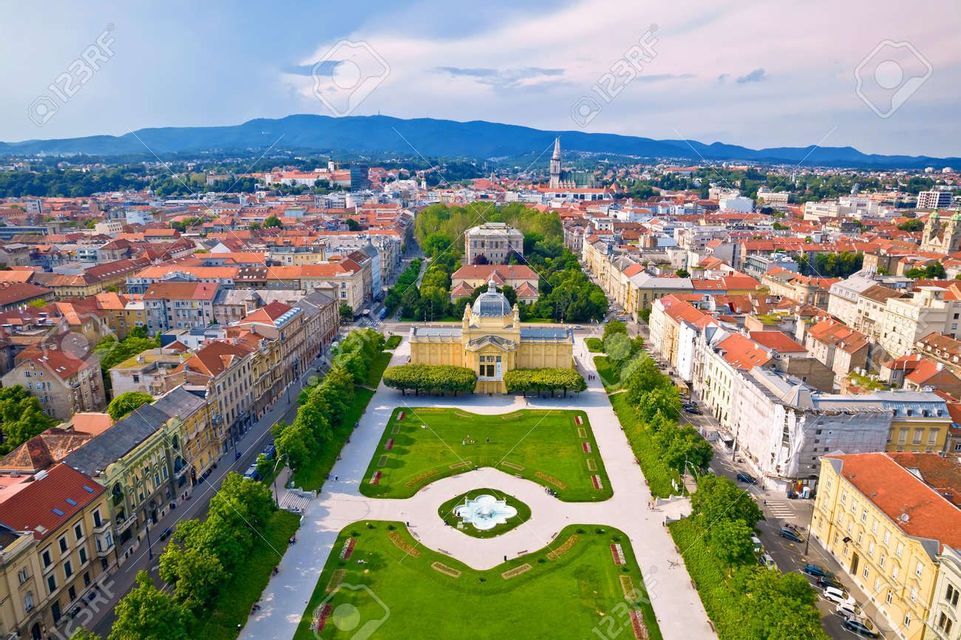 Una vista aerea di una grande città europea incentrata su un parco formale con una fontana, che conduce a un grande edificio giallo con una cupola.