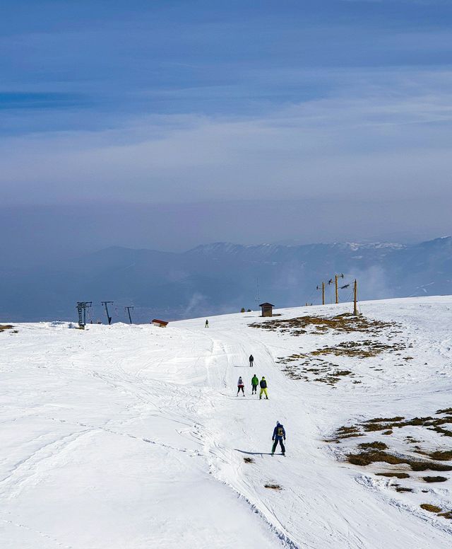 Sciatori e snowboarder su un'ampia pista innevata in montagna sotto un cielo velato.