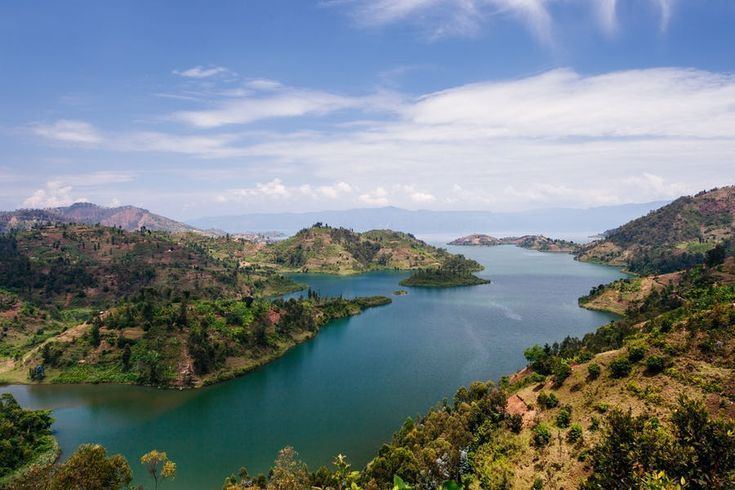Una vista elevata di un ampio lago blu che serpeggia tra dolci colline coperte di vegetazione verde sotto un cielo parzialmente nuvoloso.