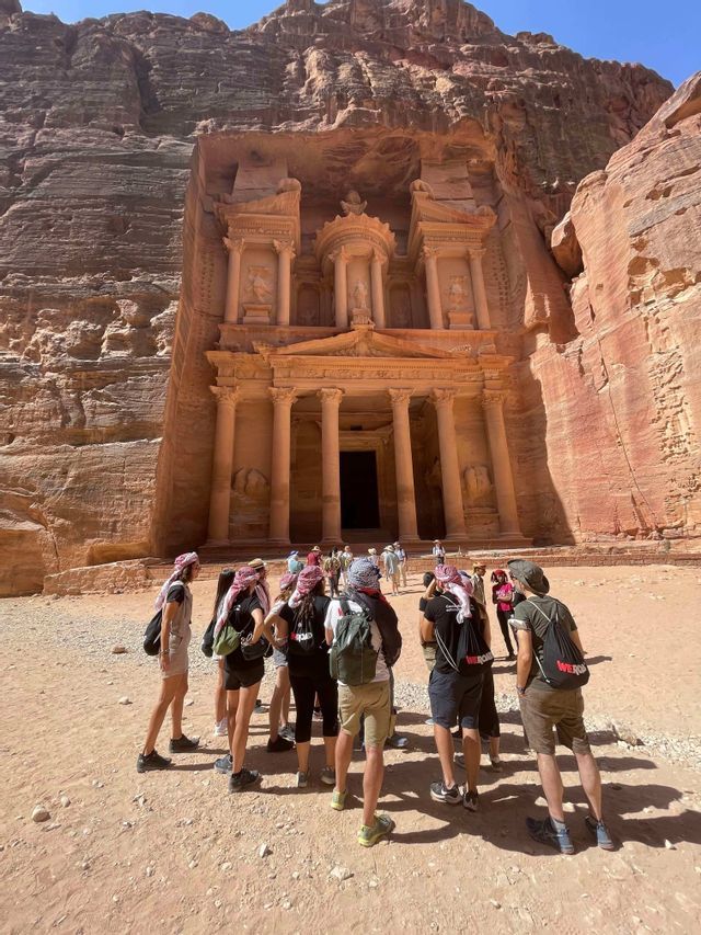 Eine WeRoad-Gruppenreise steht zusammen und blickt auf ein großes, in eine rote Felswand gehauenes Monument.