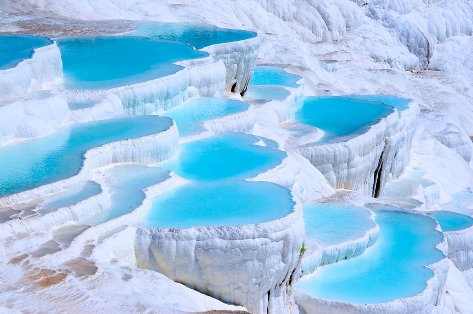 Terraced pools of bright blue water cascade down white mineral deposits, creating a layered landscape.