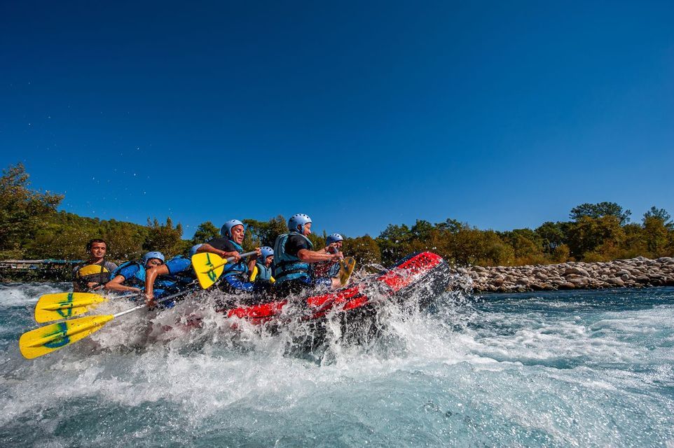 A WeRoad group trip paddling through white water rapids in a red inflatable raft under a clear blue sky.