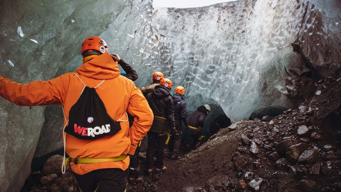 Un groupe WeRoad en voyage, casques et vestes chaudes, progresse en file indienne dans une étroite grotte de glace.