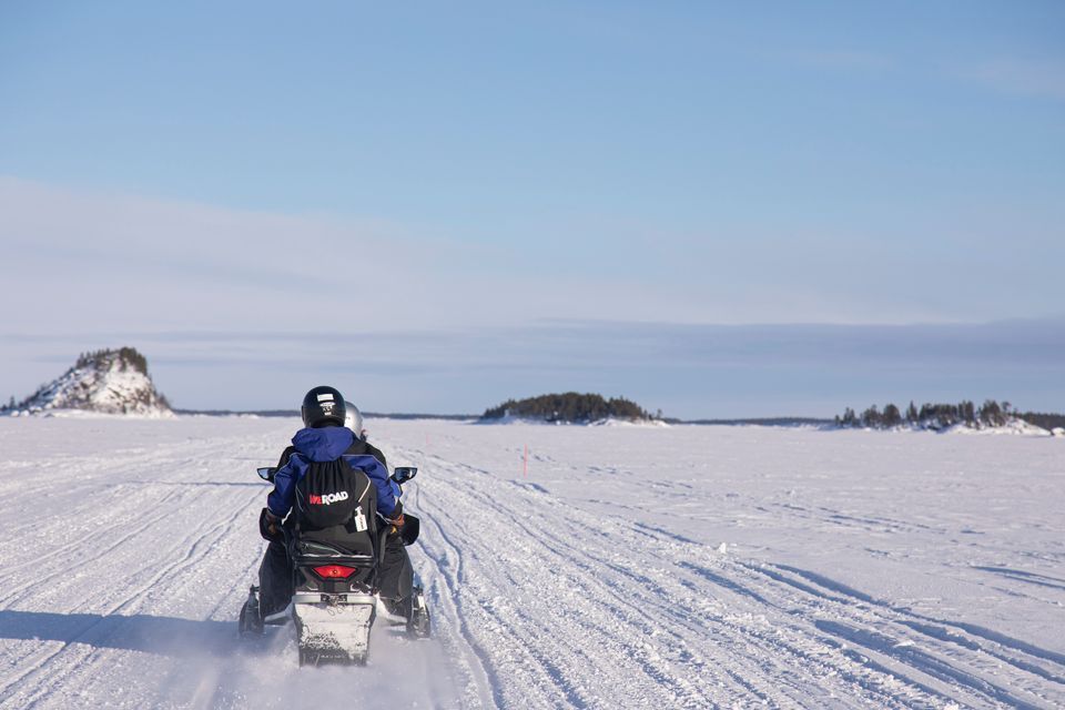 Vista da dietro di due persone di un gruppo WeRoad in motoslitta su un vasto paesaggio innevato sotto un cielo azzurro e limpido.