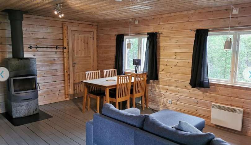 L'interno di una baita in legno con un tavolo da pranzo, un divano blu e una stufa a legna.