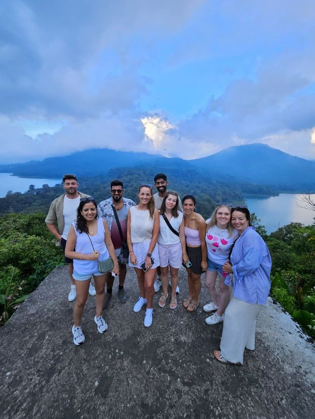 Un voyage de groupe WeRoad de neuf personnes posant sur un point de vue surplombant un lac et des montagnes luxuriantes sous un ciel nuageux.